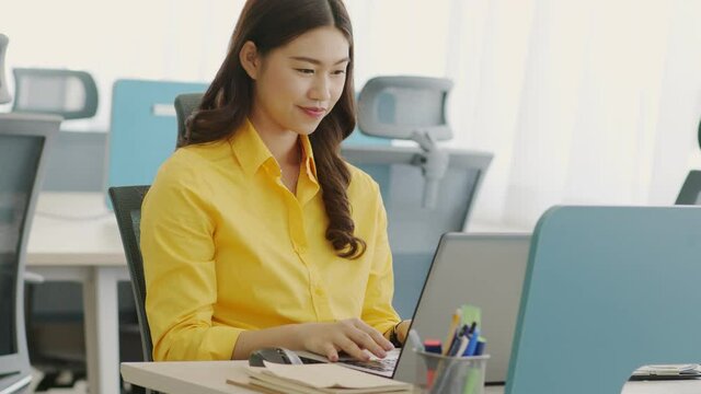 Happiness Attractive Asian woman in yellow shirt working with computer laptop thinking to get ideas and requirement in Business startup at modern office or Co-working space,Business Startup Concept