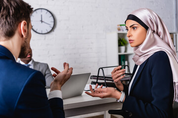 arabian businesswoman gesturing during meeting with multicultural partners, blurred foreground