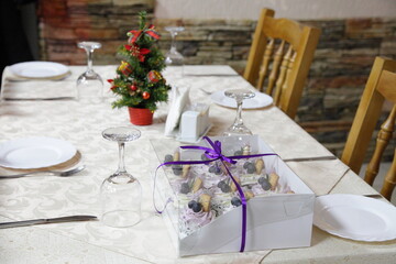 Restaurant table with cake gift, pine tree on white tablecloth and wooden chairs in empty hall, holiday in European winter cafe interior