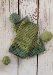 Fototapeta na wymiar A pair of green handmade crochet mittens with balls of yarn on a white wooden floor 