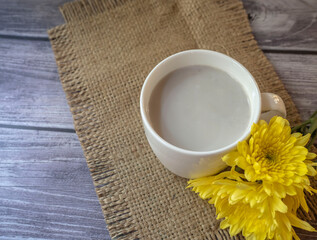 fresh homemade soy milk in white cup and yellow Chrysanthemum flower on the table,  healthy concept
