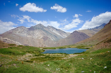 Laguna de Horcones sunny day on a hiking trail. Lake in Andes mountains with green grass around. Blue sky with clouds over hills. Aconcagua Provincial Park, Mendoza province, Argentina