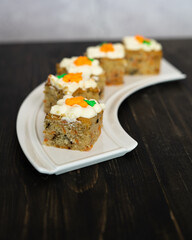 pieces of carrot cakes squares with walnuts and icing cream on a wooden background. selective focus.