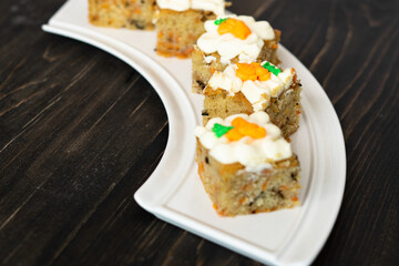 pieces of carrot cakes squares with walnuts and icing cream on a wooden background. selective focus.