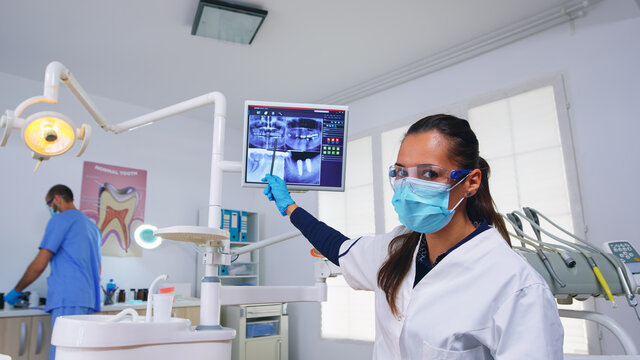 Dentist doctor and patient looking at digital teeh x-ray in dental office, person pov. Stomatology wearing protective face mask and gloves pointing at teeth radiography in stomatological clinic
