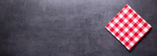Folded checked or checkered tablecloth at stone surface of table. Panorama of cloth napkin texture background