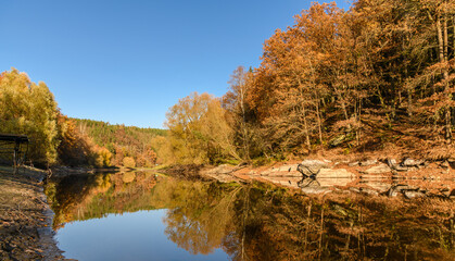 rocks and trees in autumn colors reflection in water of river