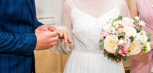 Obraz na płótnie Canvas Groom wears bride a wedding ring Bride hand holds a beautiful wedding bouquet.