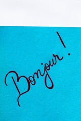 Bonjour (good morning) handwriting text close up isolated on blue paper with copy space. Writing text on memo post reminder © Vlad Ispas