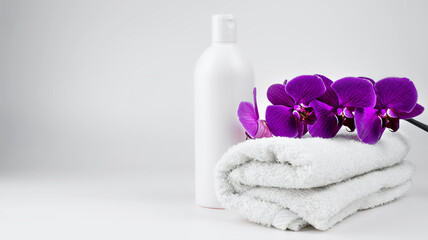 Fototapeta na wymiar a light rolled towel and a white jar of cream soap. Purple orchid branch on a towel.