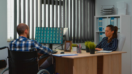 Businesswoman analysing financial statistics talking with handicapped coworker sitting in wheelchair checking graphs on desk in building office. Disabled businessman using modern technology