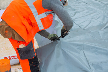 Geste metier d'un ouvrier découpant un polyane sur un chantier