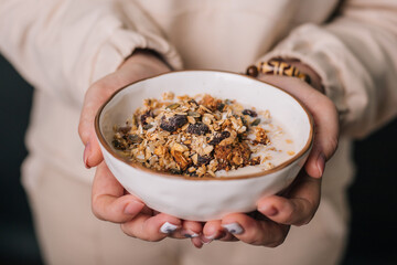 The girl's hands are holding a deep dish with breakfast. Oatmeal, nuts and raisins with milk in a cup. Diet food.