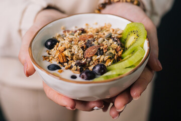 In the hands of the girl lies a deep dish with breakfast. Oatmeal, nuts and raisins with milk in a cup and slices of fresh kiwi. Diet food.