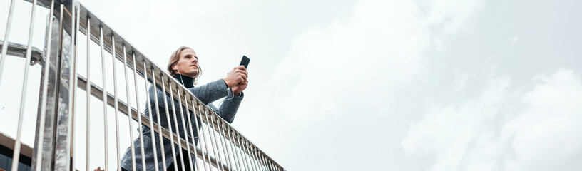 Modern businessman with smartphone on a city street. Handsome man wearing earphones and speaking on mobile phone, listening music or podcast outdoors.