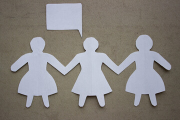 Silhouette of three girls in dresses holding hands, cut out of white paper. With speech-bubble. In the center of the photo on a beige background