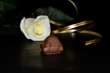 Obraz na płótnie Canvas The studio white rose with golden ribbon on a black background. Chocolate candy.