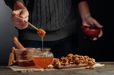 Man in a sweater prepares a breakfast of walnuts and honey.