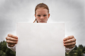 Sad serious teenager girl holding white poster with free copy space for text. Poster or paper...