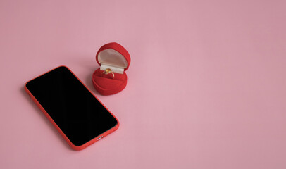 New smartphone and engagement ring in red gift box on pink background. The concept of best gift for Valentine's Day, birthday, International Women's day and other holidays. Copy space