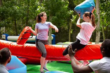 Cheerful adult women having fun on inflatable pillow fight arena in outdoor amusement park