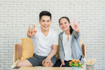 Asian couple smiling and showing I LOVE YOU gesture in sign language with looking to camera in...