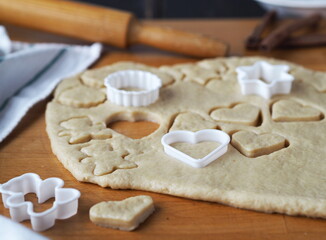 Fototapeta na wymiar Raw shortbread cookies cut from a layer of dough with cookie cutters on a kitchen board on a dark wooden table.Confectionery background.