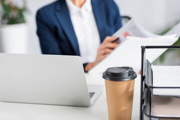 paper cup near laptop on desk with businesswoman on blurred background