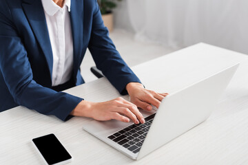 cropped view of team leader typing on laptop keyboard near smartphone with blank screen