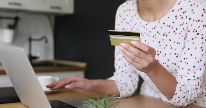Close up young woman holding credit plastic banking card, entering cvv code in computer application, confirming money transaction or activating e-banking personal account, online payments concept.