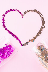 Heart shape made of multicolored glitter. Two champagne glasses with splash of heart shaped confetti over pink background. Valentine's Day concept. Flat lay