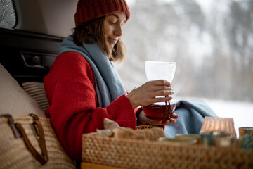 Woman brewing a coffee in car trunk in winter forest