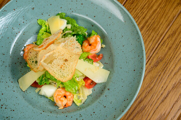 Caesar salad with shrimp on blue plate on wooden background