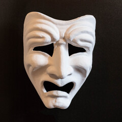 White theatrical mask with the emotion of Tragedy on a black background.