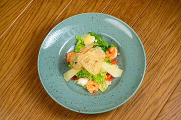 Caesar salad with shrimp on blue plate on wooden background