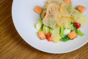 Caesar salad with salmon on white plate on wooden background