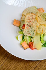 Caesar salad with salmon on white plate on wooden background