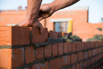 Bricklayer worker installing brick masonry on exterior wall