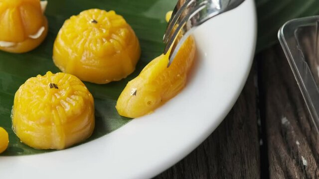 Fork is dipping into the dessert Thong-Eek, Sane Chan and Kanom Jamongkut (Thai sweets) on a white plate with banana leaves.