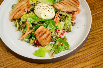 Caesar salad with croutons, quail eggs, cherry tomatoes and grilled chicken in wooden table