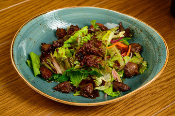 Salad with fried mushrooms, tomatoes and lettuce on a wooden table