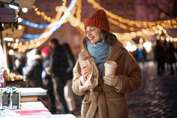 Woman with coffee staying near shopcase in the Christmas market