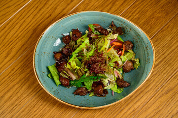 Salad with fried mushrooms, tomatoes and lettuce on a wooden table