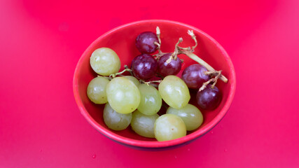 Fresh red and green grapes in a bowl isolated on pink background. Selective focus on the fresh red grapes.