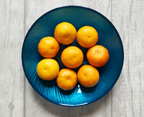 Blue plate with sweet tangerines on wooden grey background. From above, flat lay.  Food background.