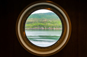 Fototapeta na wymiar Porthole window view along the Inside Passage cruise, Vancouver island, British Columbia, Canada. Focus on landscape.