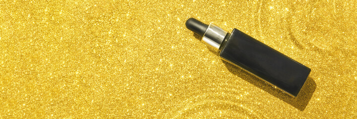 Water circle with gold sparkles background. Yellow glitter backdrop. Golden texture. Black serum bottle. Copyspace mockup. Dreamy shiny design detail. Medical drop
