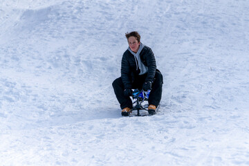 Fototapeta na wymiar A teenage boy rides a snow bike sled down a snowy hill in the mountains.