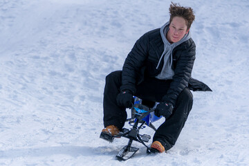 A teen boy's hair flies in the wind as he leans into a turn on a snow bike sled on a snowy mountain run.