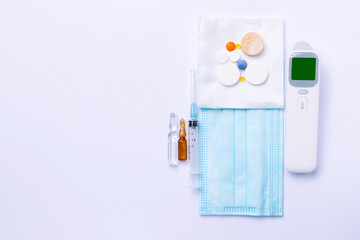 Medical equipment on a white background. Non-contact thermometer, medicines, syringe and ampoules. View from above.